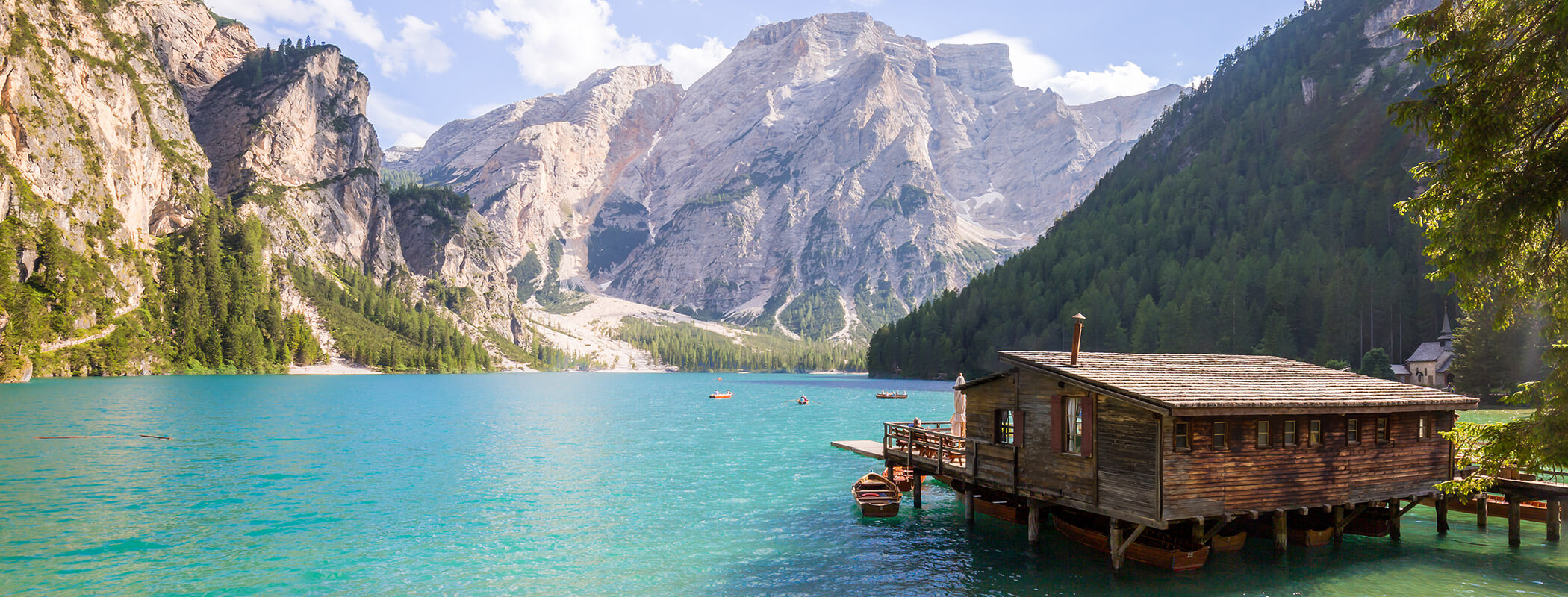 Holzhütte am türkisfarbenen See, umgeben von Kiefern und hohen, felsigen Bergen unter blauem Himmel. - Ansitz Toldt Dolomites Village