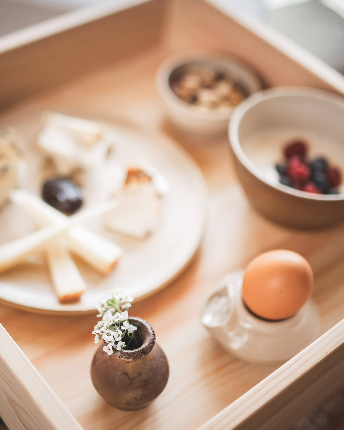 Holztablett mit Käse, Beeren, Nüssen, einem Ei und einer kleinen Vase mit weißen Blumen. - Ansitz Toldt Dolomites Village