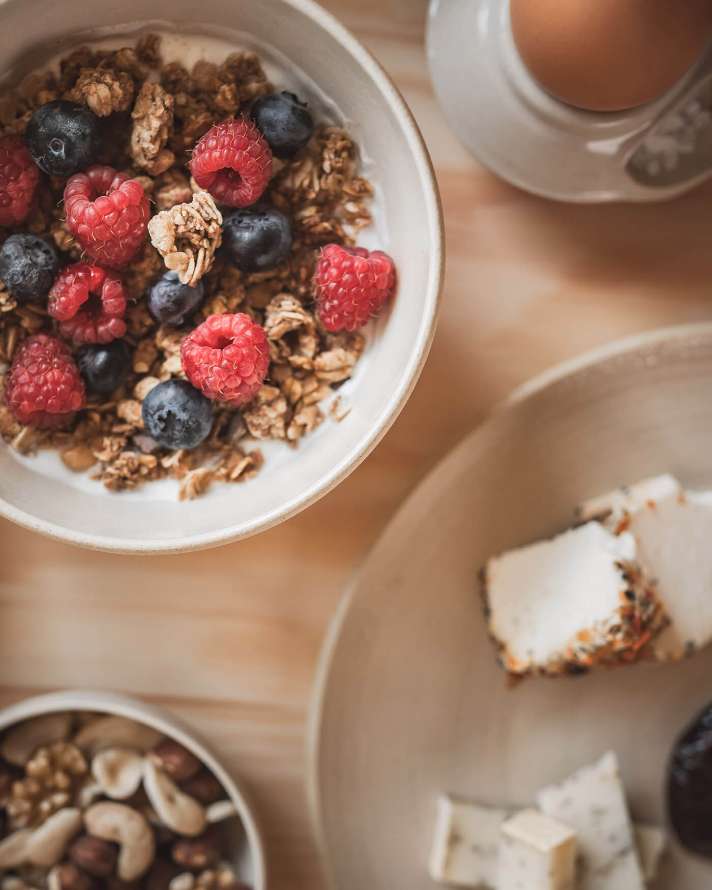 Schale mit Müsli mit Himbeeren und Heidelbeeren, Nüssen, Käse und einem gekochten Ei auf einem Holztisch. - Ansitz Toldt Dolomites Village