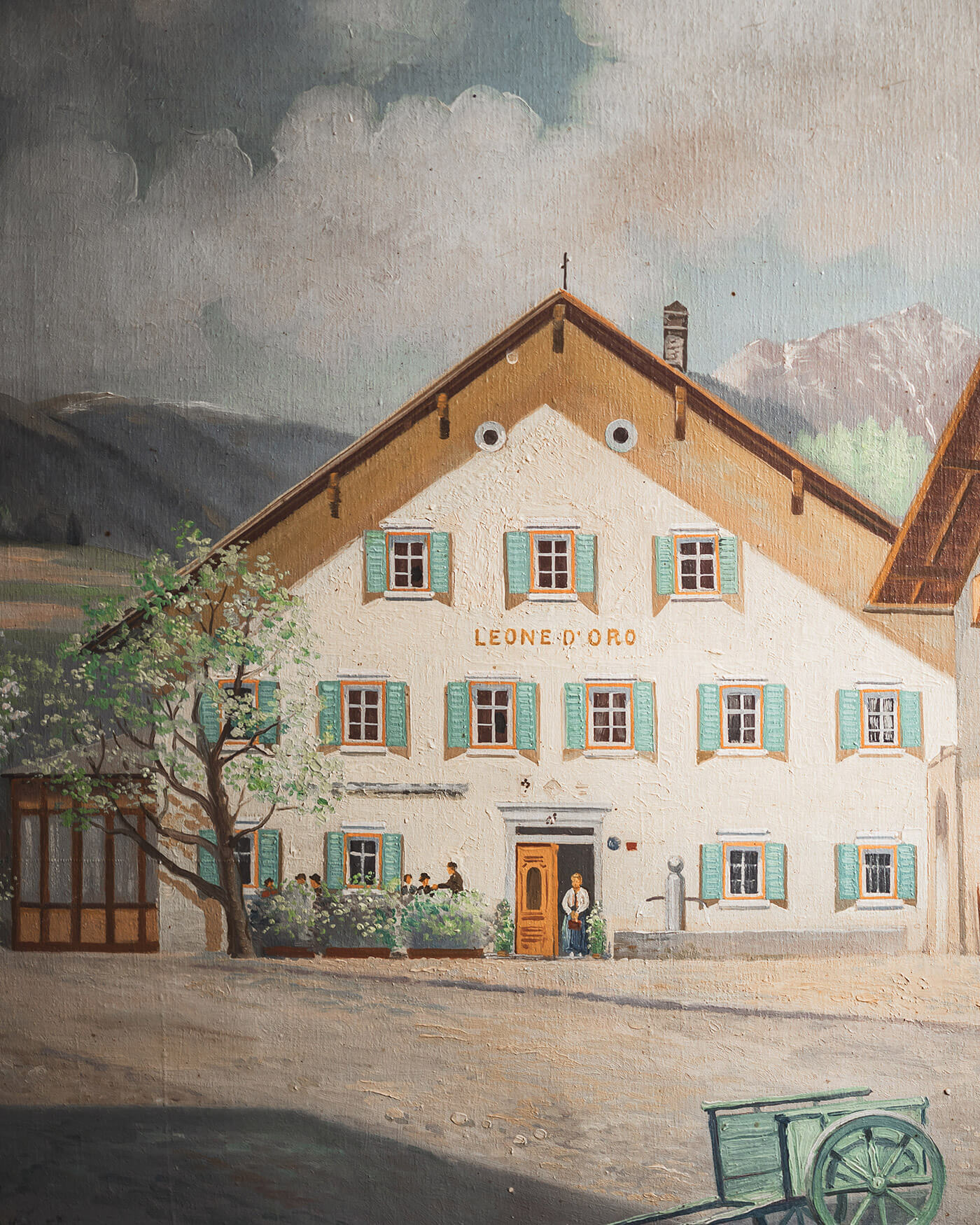 Gemälde eines rustikalen Hauses mit grünen Fensterläden, beschriftet mit Leone DOro, mit Menschen, die vor dem Eingang stehen. - Ansitz Toldt Dolomites Village