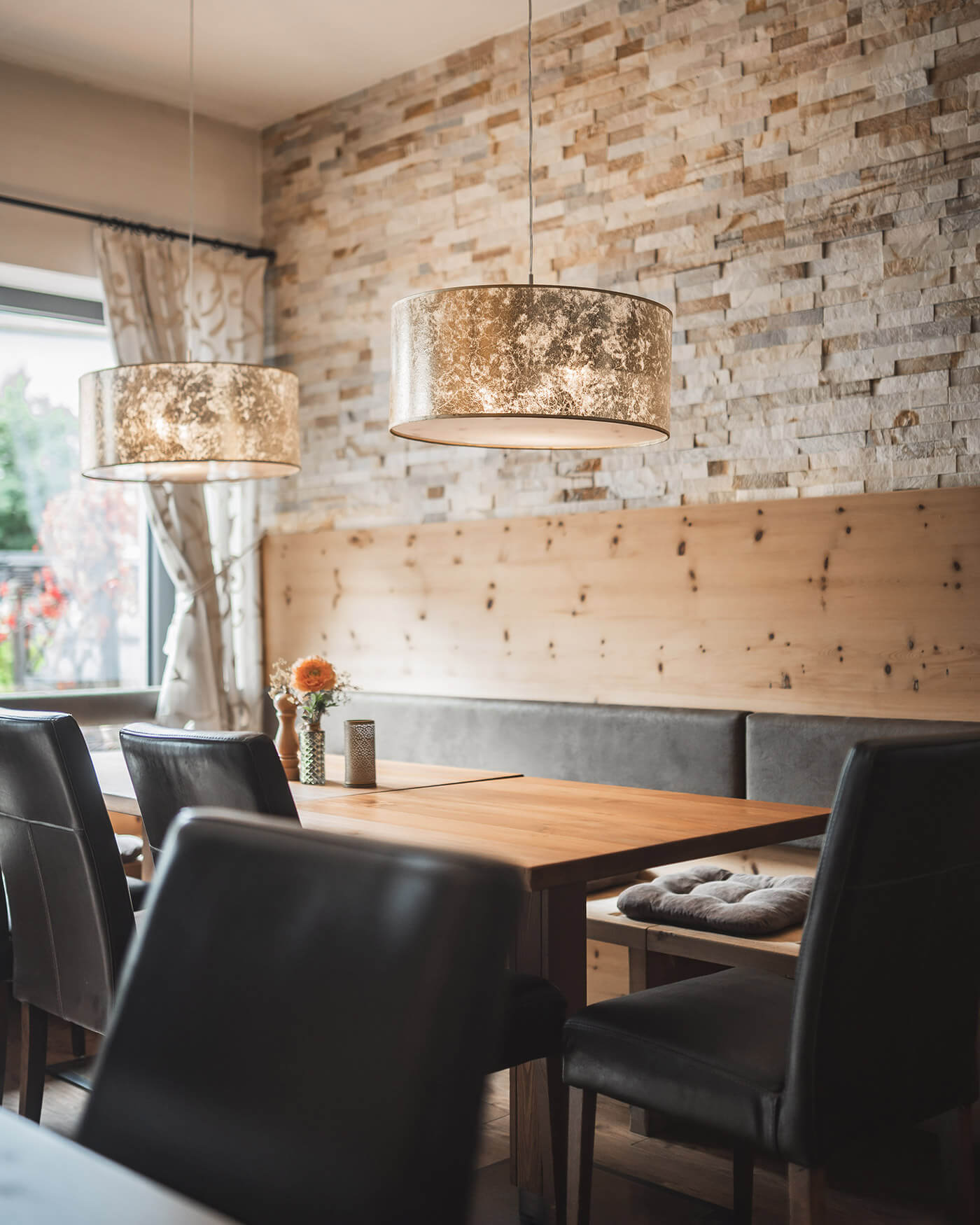 Cozy dining area with wooden table, black chairs, pendant lights, and a stone accent wall. - Ansitz Toldt Dolomites Village