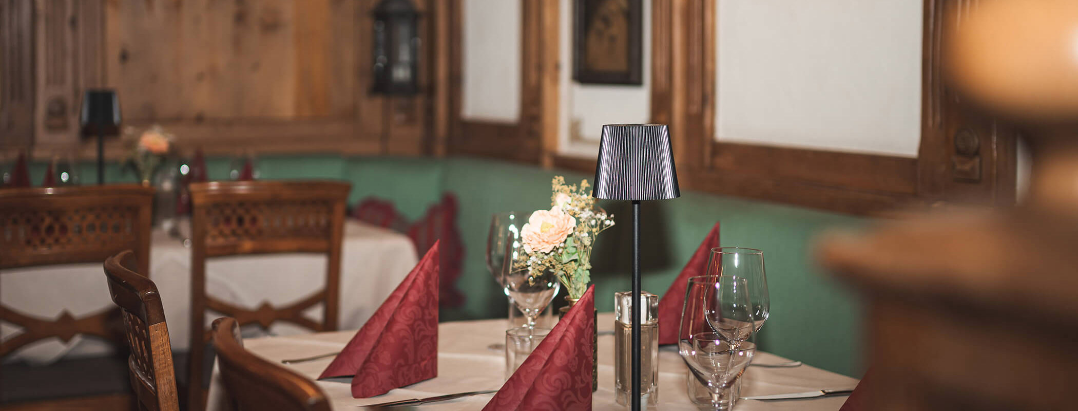Eleganter Restauranttisch mit roten Servietten, Gläsern und einem blumigen Tafelaufsatz in einem gemütlichen, holzgetäfelten Raum. - Ansitz Toldt Dolomites Village