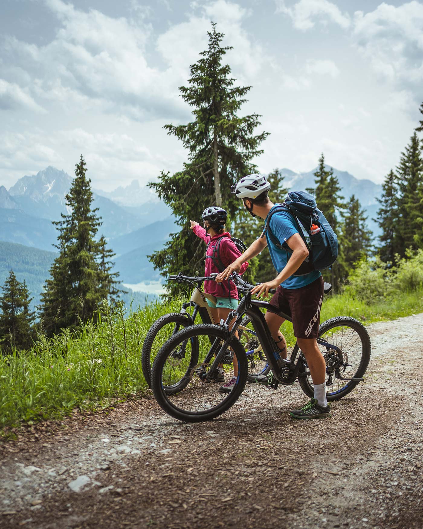 Zwei Radfahrer machen auf einem Waldweg eine Pause und betrachten die Berge in der Ferne bei bewölktem Himmel. - Ansitz Toldt Dolomites Village