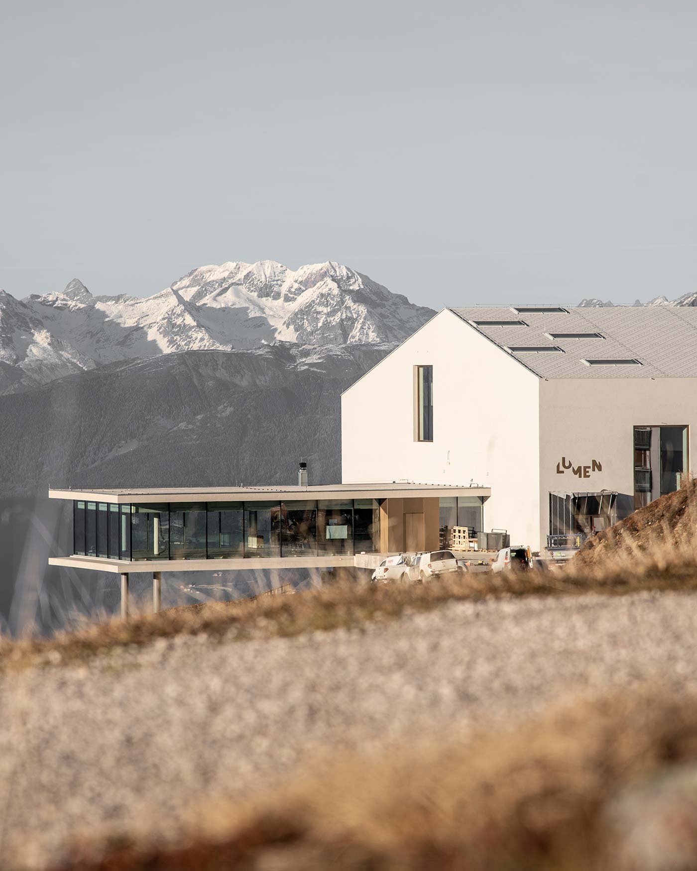 Modernes Gebäude mit LUMEN-Schild vor schneebedeckten Bergen und klarem Himmel im Hintergrund. - Ansitz Toldt Dolomites Village