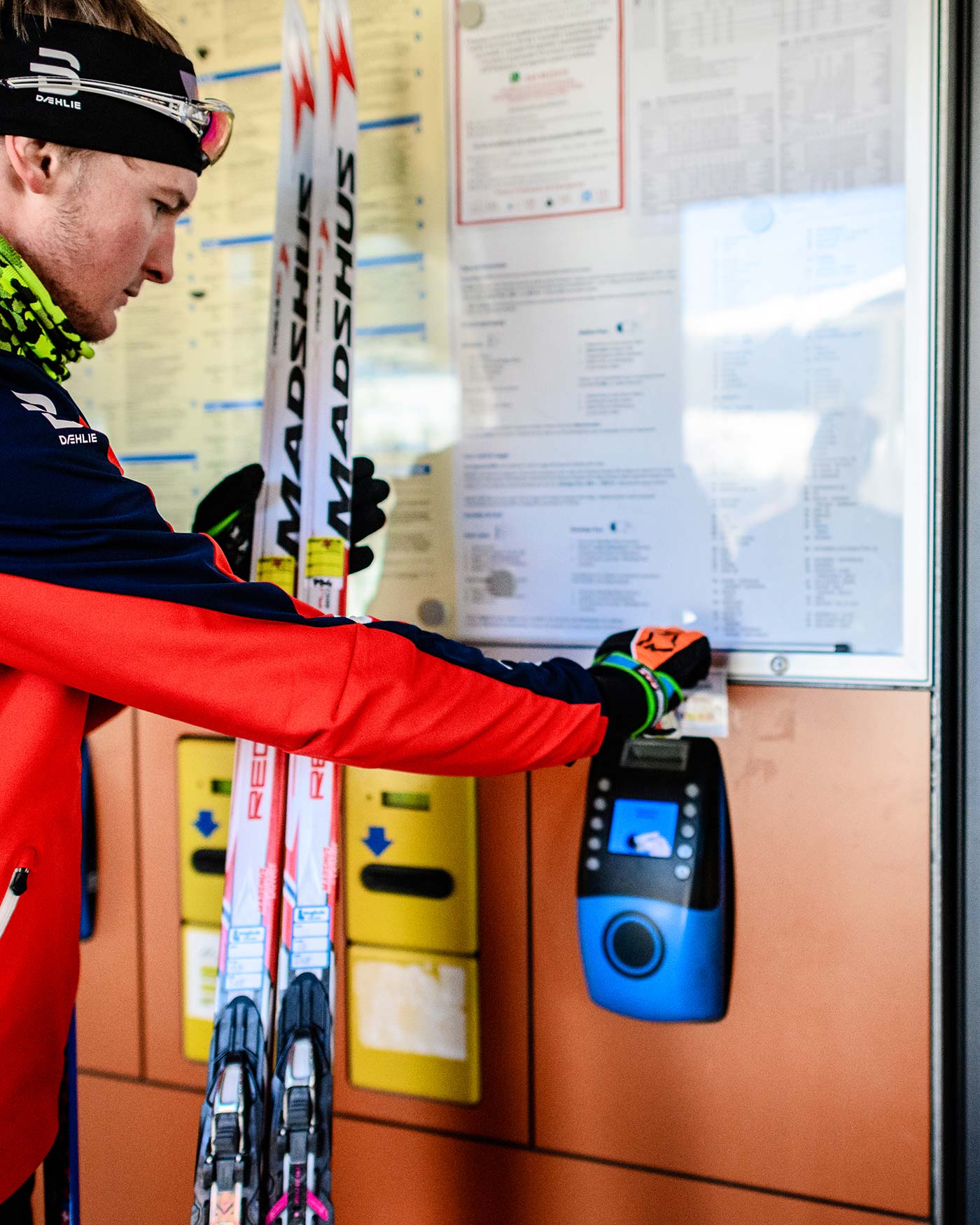 Ein Skifahrer in Rot scannt eine Karte an einem Fahrkartenautomaten, während er die Skier in der Halle hält. - Ansitz Toldt Dolomites Village