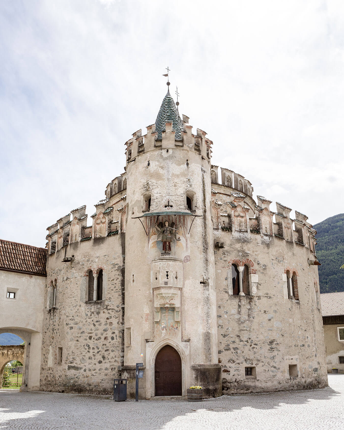 Mittelalterliches Steingebäude mit rundem Turm, bogenförmigem Portal und dekorativen Fresken über dem Eingang. - Ansitz Toldt Dolomites Village