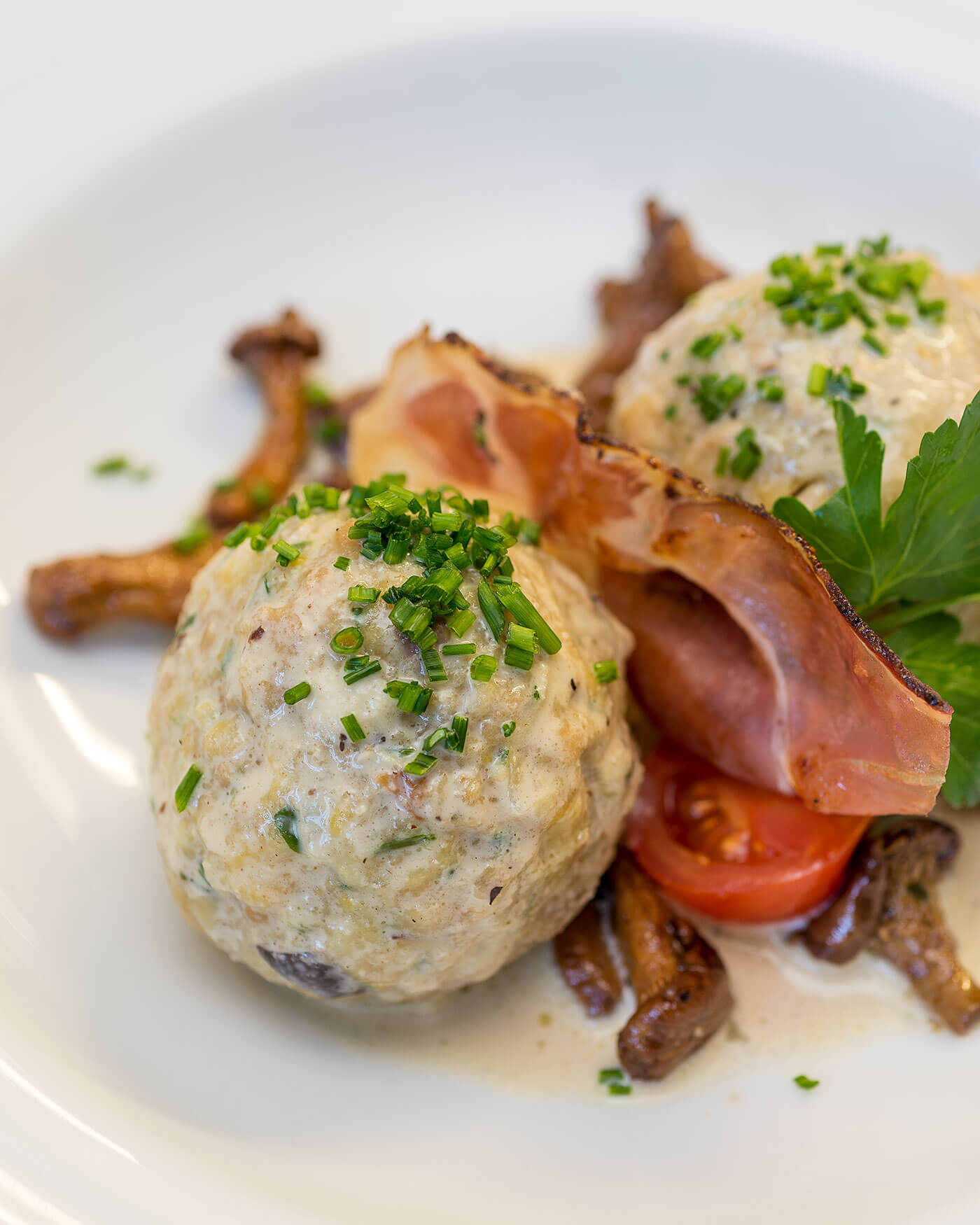 Zwei mit Schnittlauch belegte Semmelknödel, serviert mit Champignons, Tomatenscheiben und einer Scheibe Schinken. - Ansitz Toldt Dolomites Village