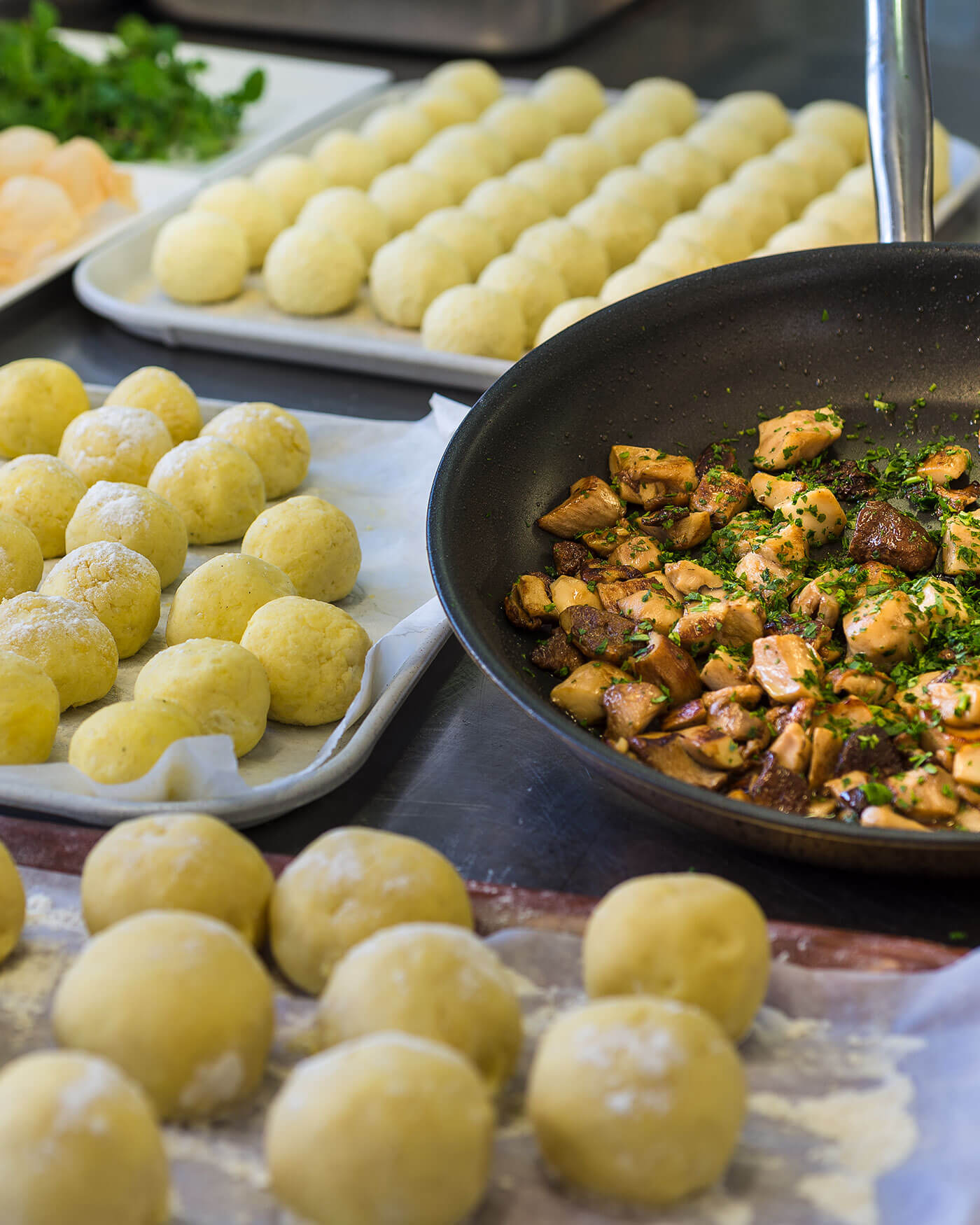 Rohe Knödel auf Tabletts und eine Pfanne mit gekochtem Huhn und Kräutern auf einem Küchentisch. - Ansitz Toldt Dolomites Village