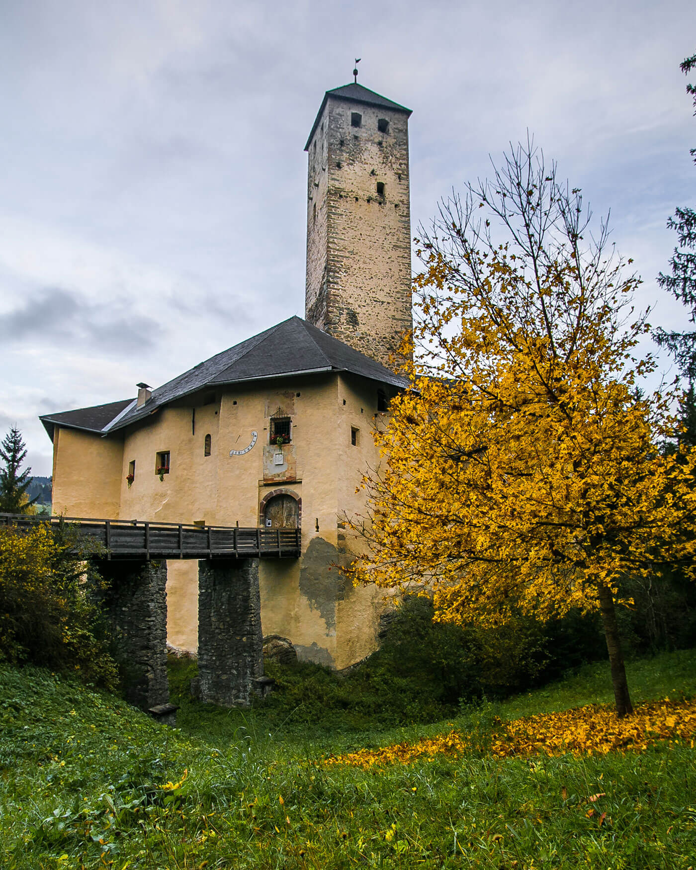 Mittelalterliche Steinburg mit einem hohen Turm, einer Holzbrücke und einem gelbblättrigen Baum im Herbst. - Ansitz Toldt Dolomites Village