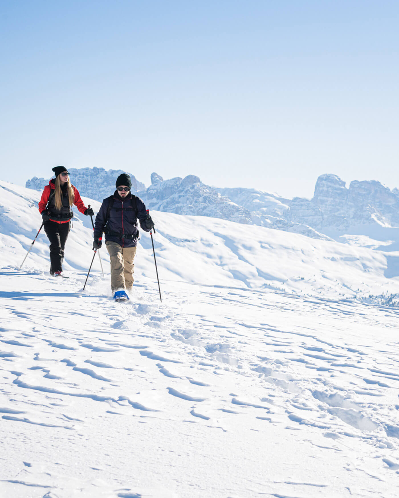 Zwei Menschen, die in einer verschneiten Berglandschaft unter blauem Himmel Schneeschuhwandern. - Ansitz Toldt Dolomites Village