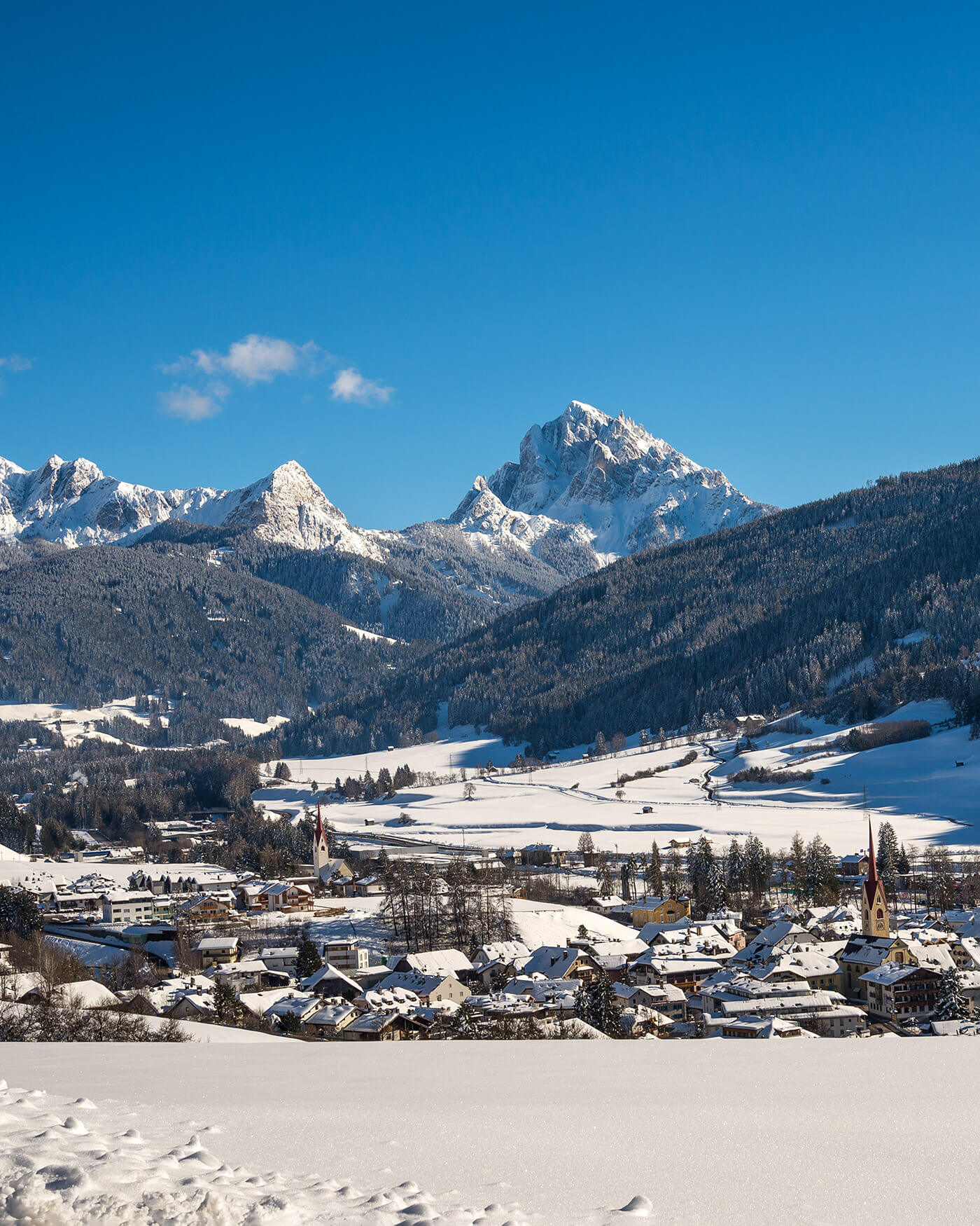 Verschneites Alpendorf mit Bergen im Hintergrund unter einem klaren blauen Himmel. - Ansitz Toldt Dolomites Village